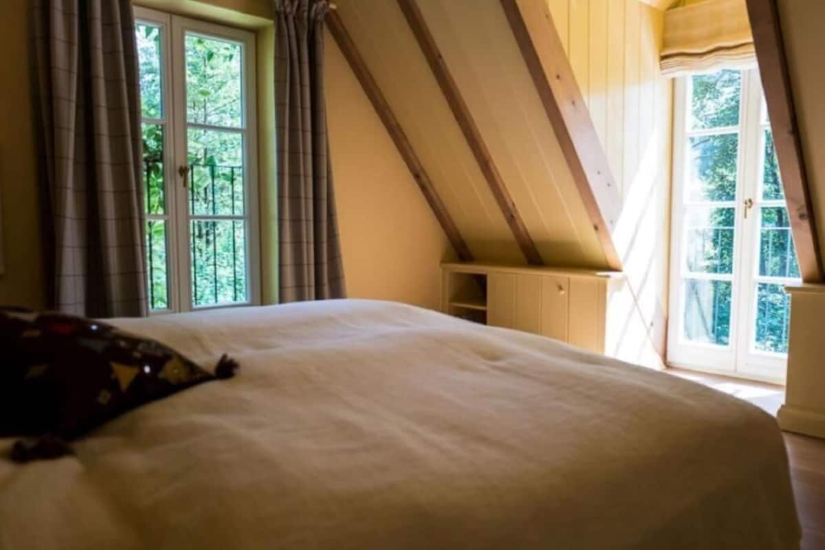 A bedroom with a large bed, wooden ceiling beams, and a window with curtains.