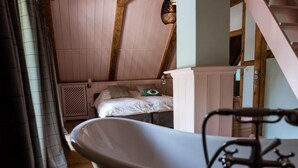 A bedroom with a sloped ceiling, a wooden beam structure, a single bed with pillows, a white radiator, and a bathtub with a faucet. - Alcor Exclusive Friedrichsruh (Aumuehle)