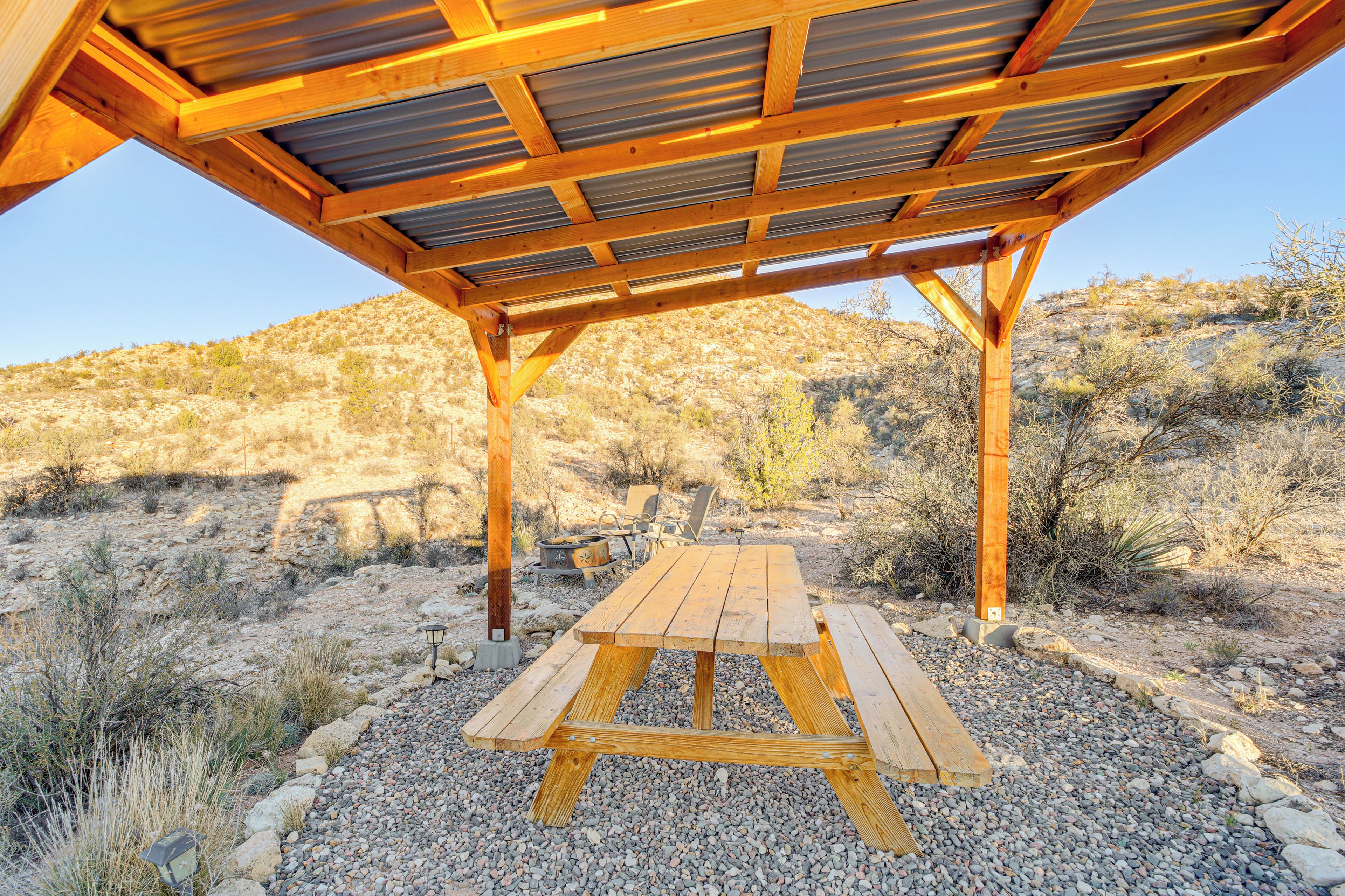 Une table de pique-nique en bois, placée sous un espace abrité, avec vue sur un paysage désertique.