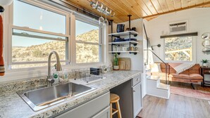 A kitchen with a granite countertop, stainless steel sink, and wooden stools. There are shelves with dishes and a cactus on the counter. - Incredible Views at Tiny Heaven In Cottonwood (Cottonwood)