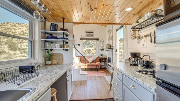 A compact kitchen with a wooden ceiling, built-in shelves, a central island, and a view of a desert landscape. - Incredible Views at Tiny Heaven In Cottonwood (Cottonwood)