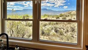 A room with a large window offering a view of a desert landscape with mountains in the distance. - Incredible Views at Tiny Heaven In Cottonwood (Cottonwood)