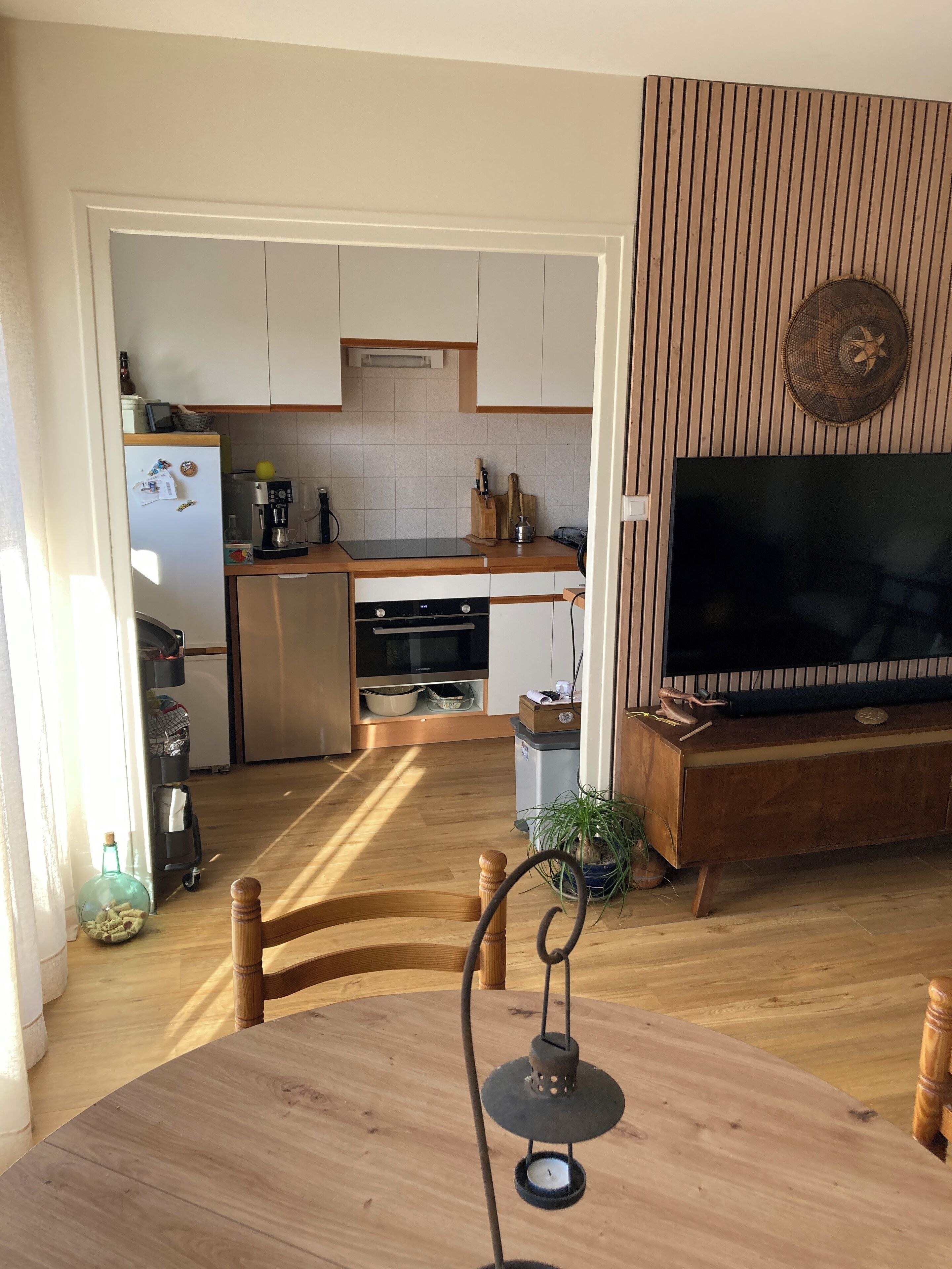 A modern kitchen with white cabinets, a built-in oven, and a coffee machine. There is a dining table with a candle in the center.