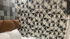 Ein Bett mit weißer Bettwäsche, einem braunen Kopfteil und einer Wand mit geometrischem Muster im Hintergrund.