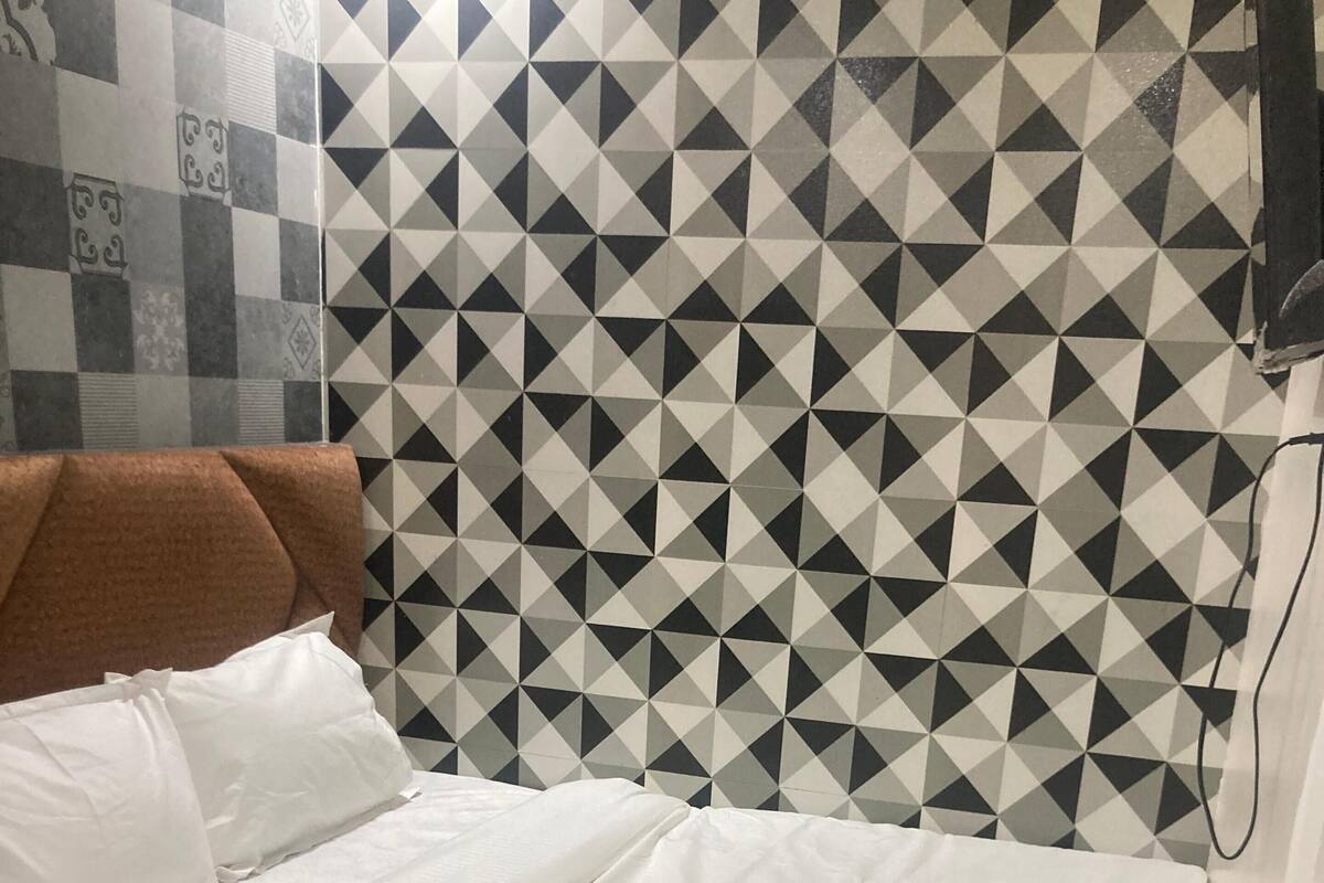Ein Bett mit weißer Bettwäsche, einem braunen Kopfteil und einer Wand mit geometrischem Muster im Hintergrund.