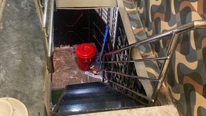 Eine schmale Treppe mit Metallhandlauf, einem roten Eimer und einem Mopp, der an der Wand lehnt.