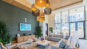 A modern lobby with a large sofa, a coffee table, and hanging wicker lamps. There are potted plants and a painting on the wall. - Saiya  804 (Phoenix)