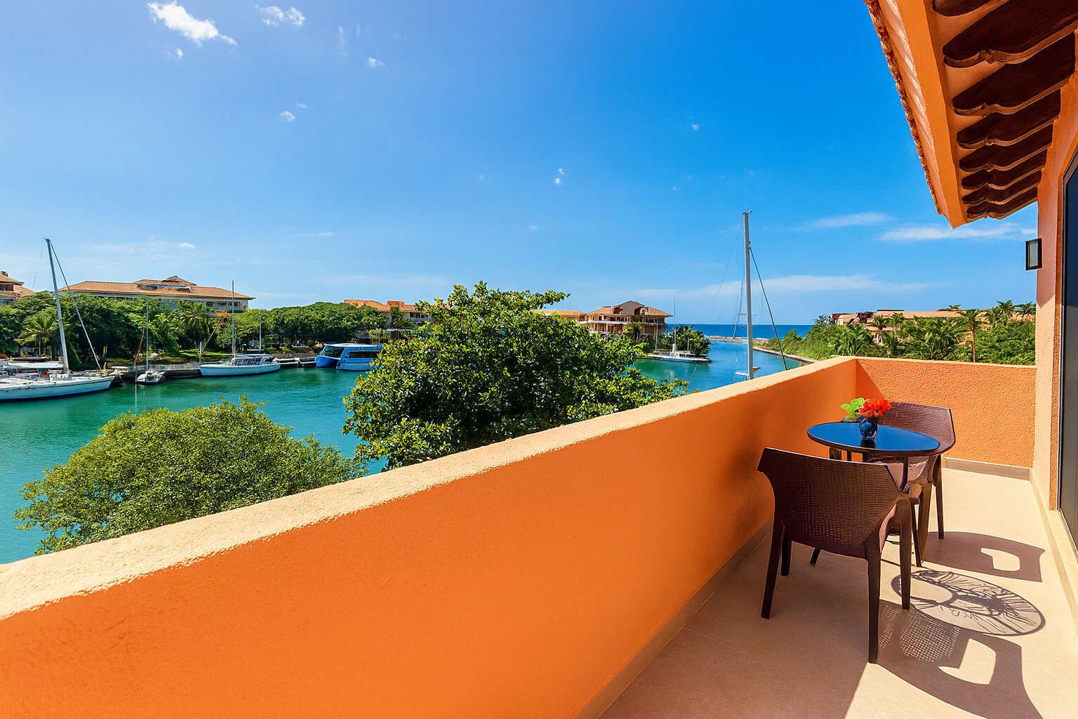 Un balcon avec une table et des chaises donnant sur une marina où l’on peut admirer des bateaux et des bâtiments.