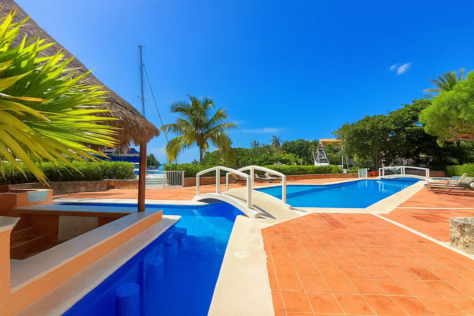 Una piscina con plataforma blanca y techo de paja.