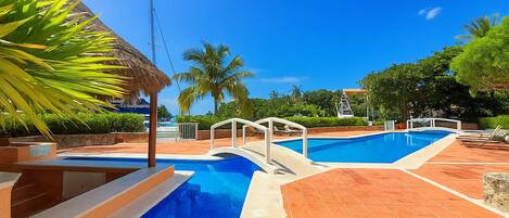 Una piscina con plataforma blanca y techo de paja.