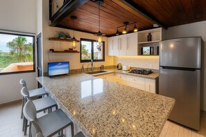 Eine moderne Küche mit Granit Arbeitsplatten, Edelstahlgeräten und Pendelleuchten.