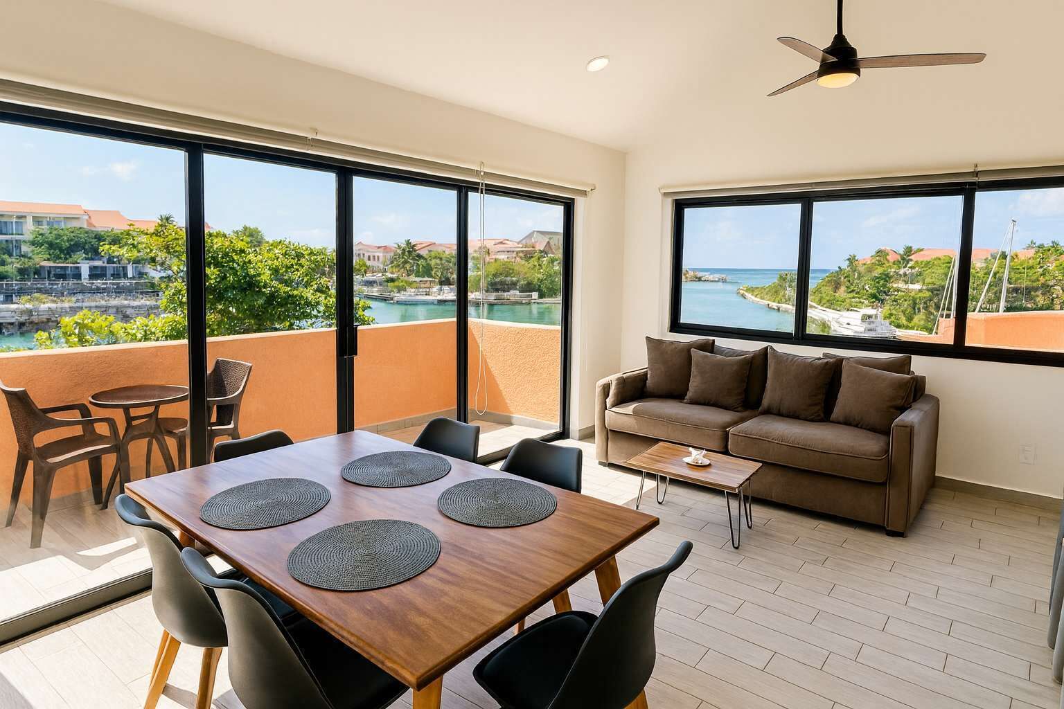 Un balcón amplio con zona de comedor, sofá y ventanas grandes con vistas a un paisaje costero.