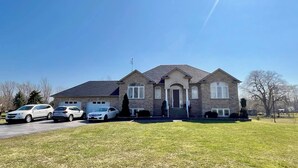 A two-story house with a garage, a driveway with three cars, and a well-maintained lawn. - Close to beach SAUNA & Movie Room/Sherkston (Port Colborne)