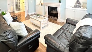 A living room with a fireplace, leather sofas, a coffee table, and a mirror on the wall. - Close to beach SAUNA & Movie Room/Sherkston (Port Colborne)