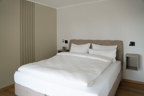 Een netjes opgemaakt bed in een kamer met een gestreepte wand, een nachtkastje en een wandlamp.