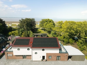 Un edificio moderno con techo rojo, paneles solares y vista a un cuerpo de agua.