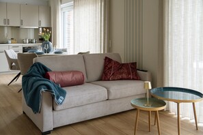 Een woonkamer met een bank, een glazen salontafel en een eethoek op de achtergrond.