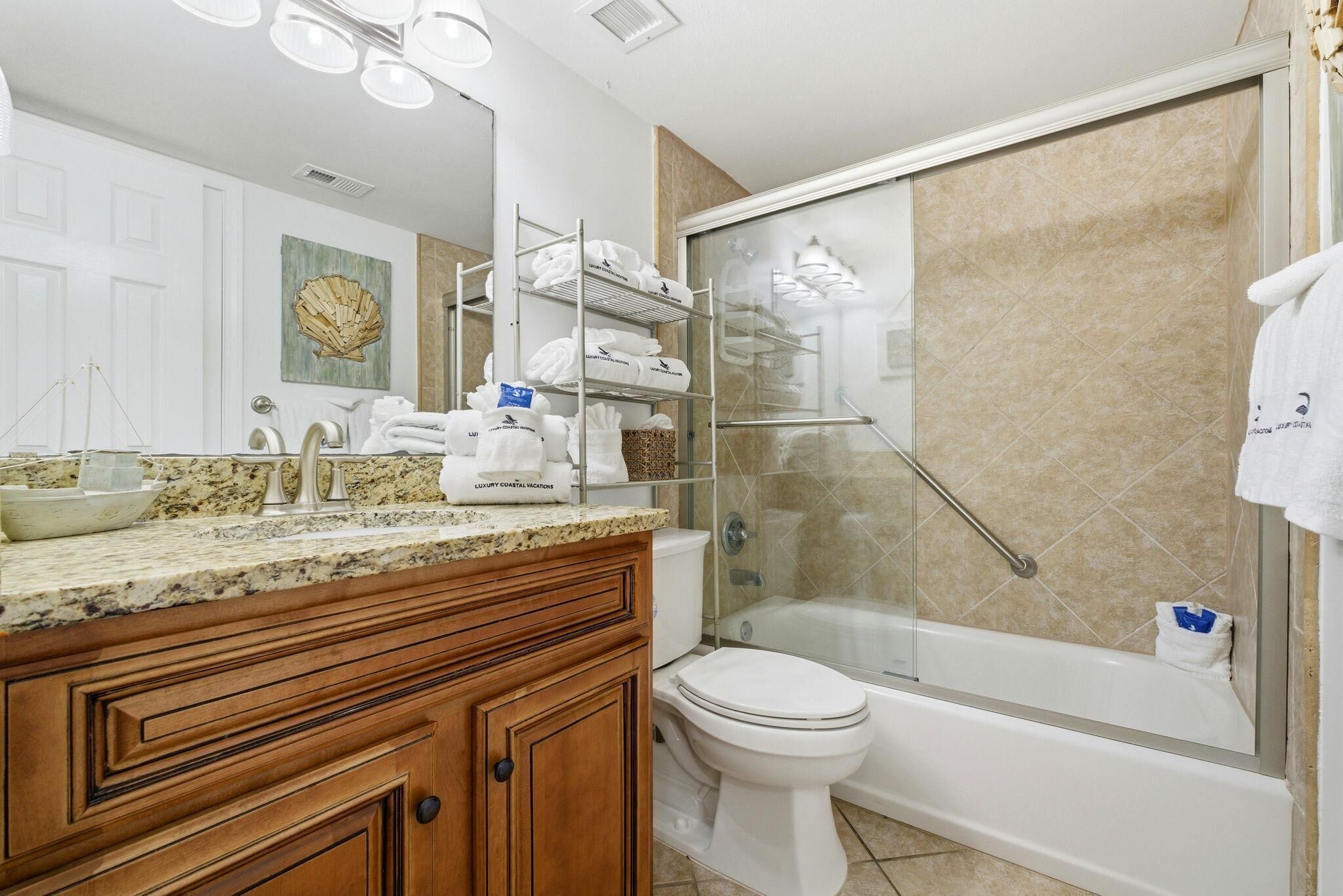 A bathroom with a granite countertop, a white toilet, a glass-enclosed shower, and a wooden vanity.