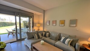 Una sala de estar moderna con un sofá gris, una mesa de centro de madera y un ventanal que da a un patio exterior.