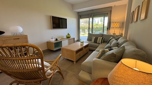 Una sala de estar moderna con sofá, mesa de comedor, televisor y ventana con vista a zonas verdes.