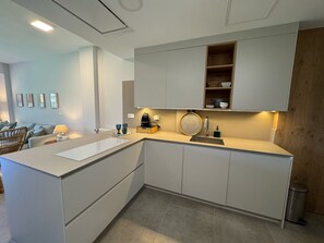 A modern kitchen with white cabinetry, a built-in island, and a wooden accent wall. - Exclusive apartment in Urb. Los Altos de El Rompido (El Rompido)