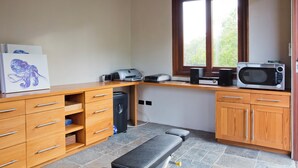 A compact kitchen with wooden cabinets, a countertop, a microwave, a coffee maker, and a bench.