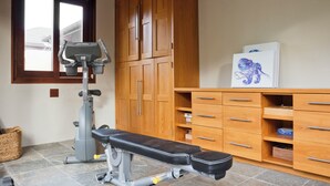 A home gym with a bench press, a stationary bike, and wooden cabinets.