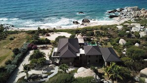 A coastal property with a large house, a swimming pool, and a beach view.