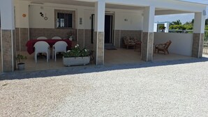 A covered outdoor area with a dining table and chairs, a seating area with a sofa, and a potted plant.