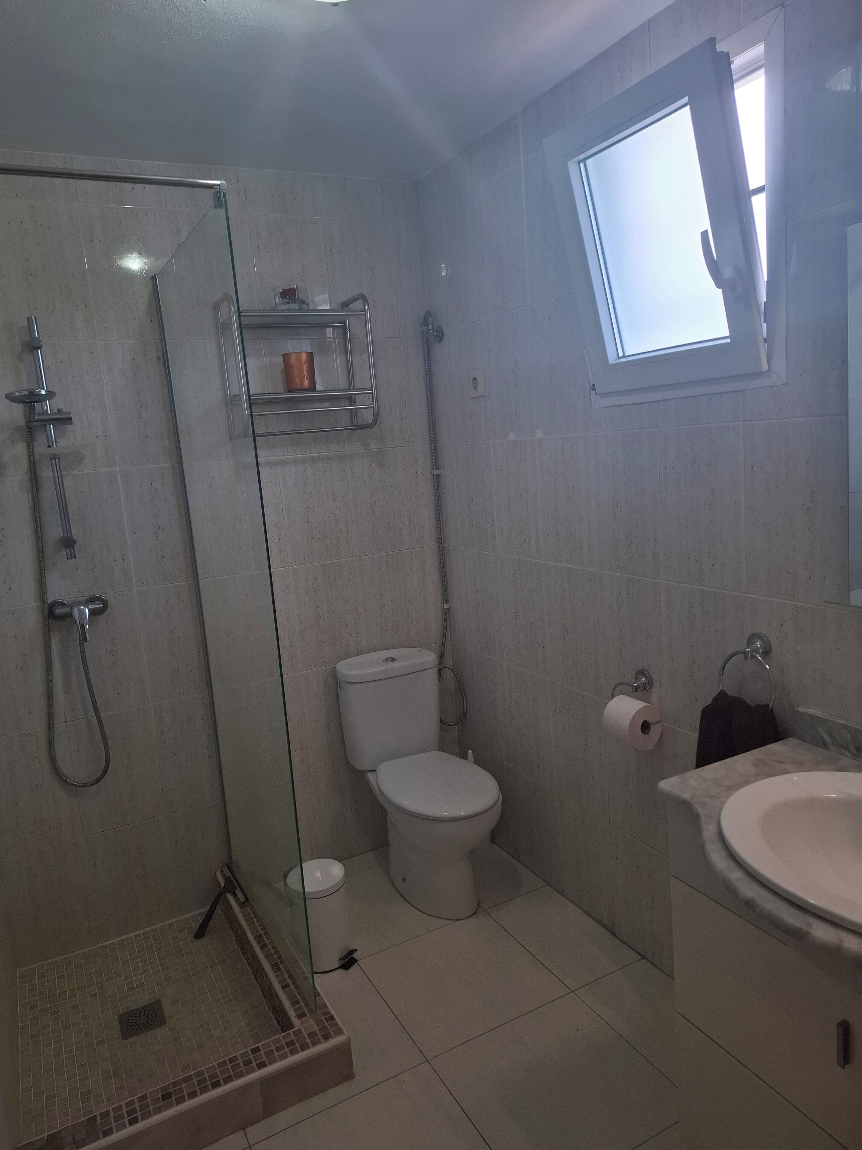 Un baño con ducha de vidrio, inodoro, lavamanos y ventana.