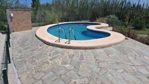 A swimming pool with a unique curved design, surrounded by stone tiles and a metal fence.