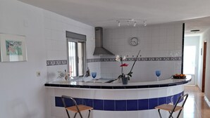 A kitchen with a curved island, two foldable chairs, a clock, and a window.