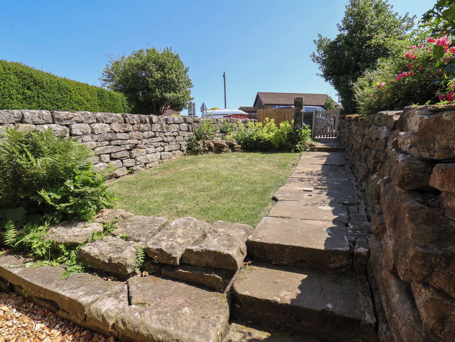 A stone wall with a grassy area and a pathway leading to a gate.