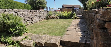 A stone wall with a grassy area and a pathway leading to a gate.