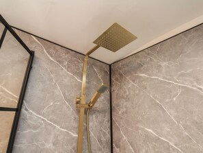 Eine moderne Dusche mit Duschkopf und Handbrause, an einer Wand mit Marmoroptik befestigt.