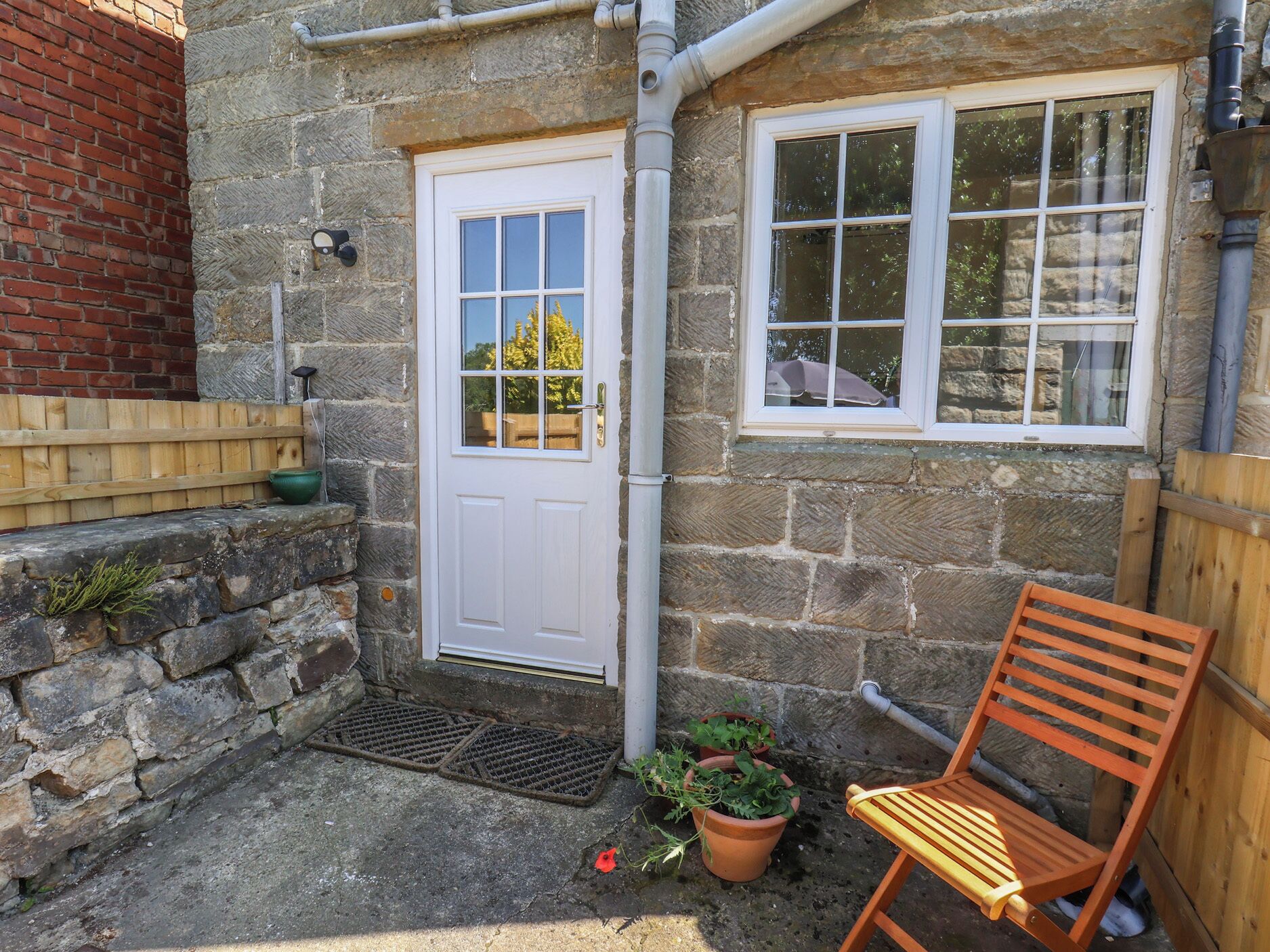 A stone building with a white door and windows, a wooden bench, and a potted plant.