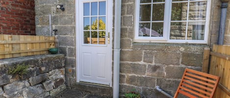 A stone building with a white door and windows, a wooden bench, and a potted plant.