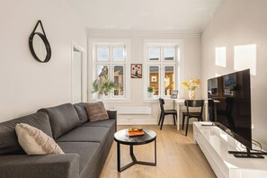 A modern living room with a grey sofa, a small round coffee table, a TV, and a dining area with a white table and chairs. - City Center Apartment - Top location (Bergen)