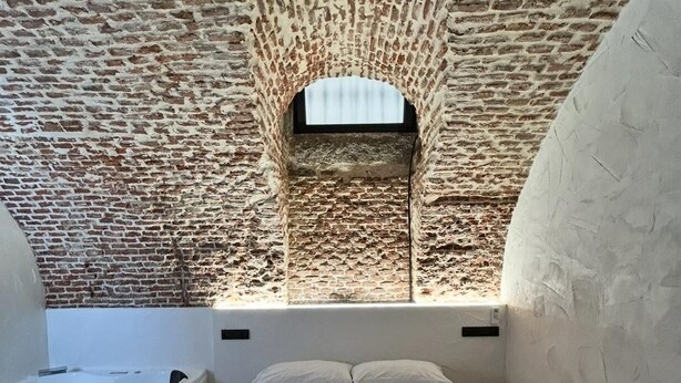 A bedroom with a brick ceiling, a bed with white bedding, and a small window. - Room 4 in the center (Madrid)