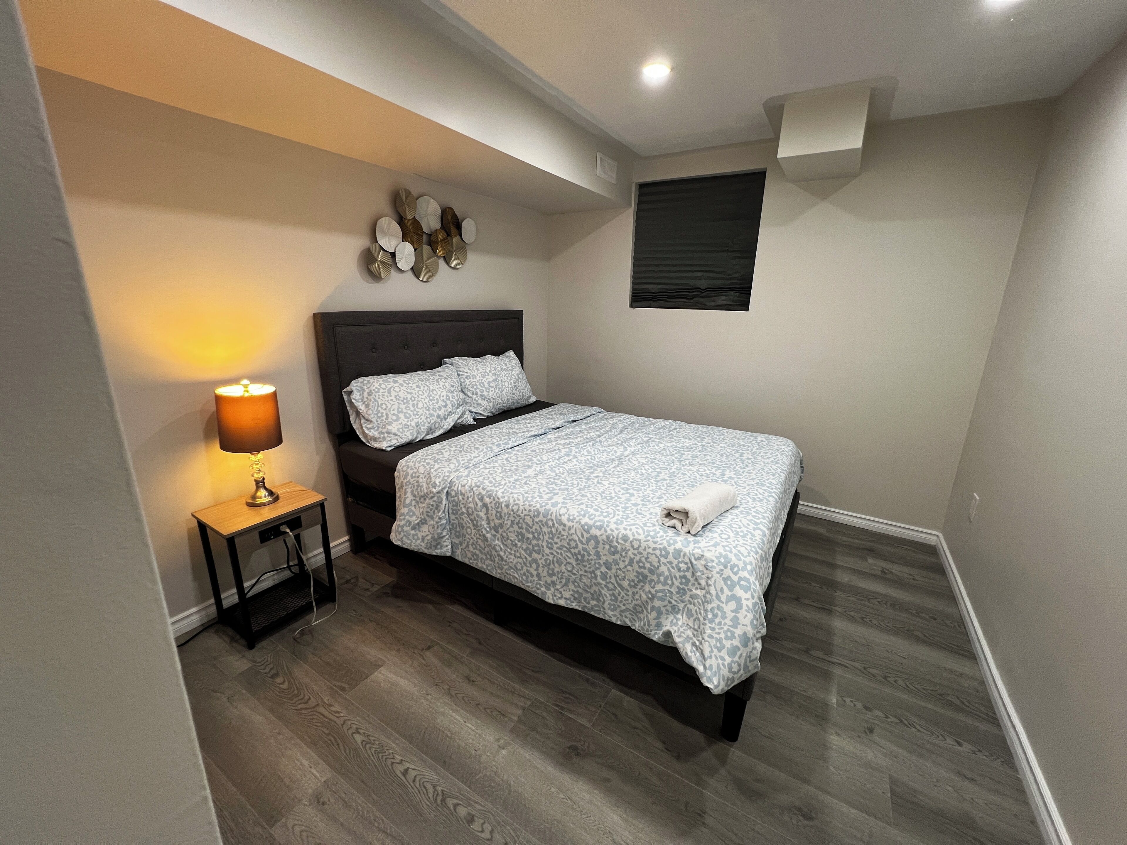 Une chambre à coucher comprenant un lit, une table de chevet, une lampe et un élément décoratif fixé au mur.