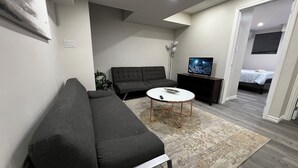 Een moderne woonkamer met een grijze bank, een ronde salontafel en een televisie op een meubel.