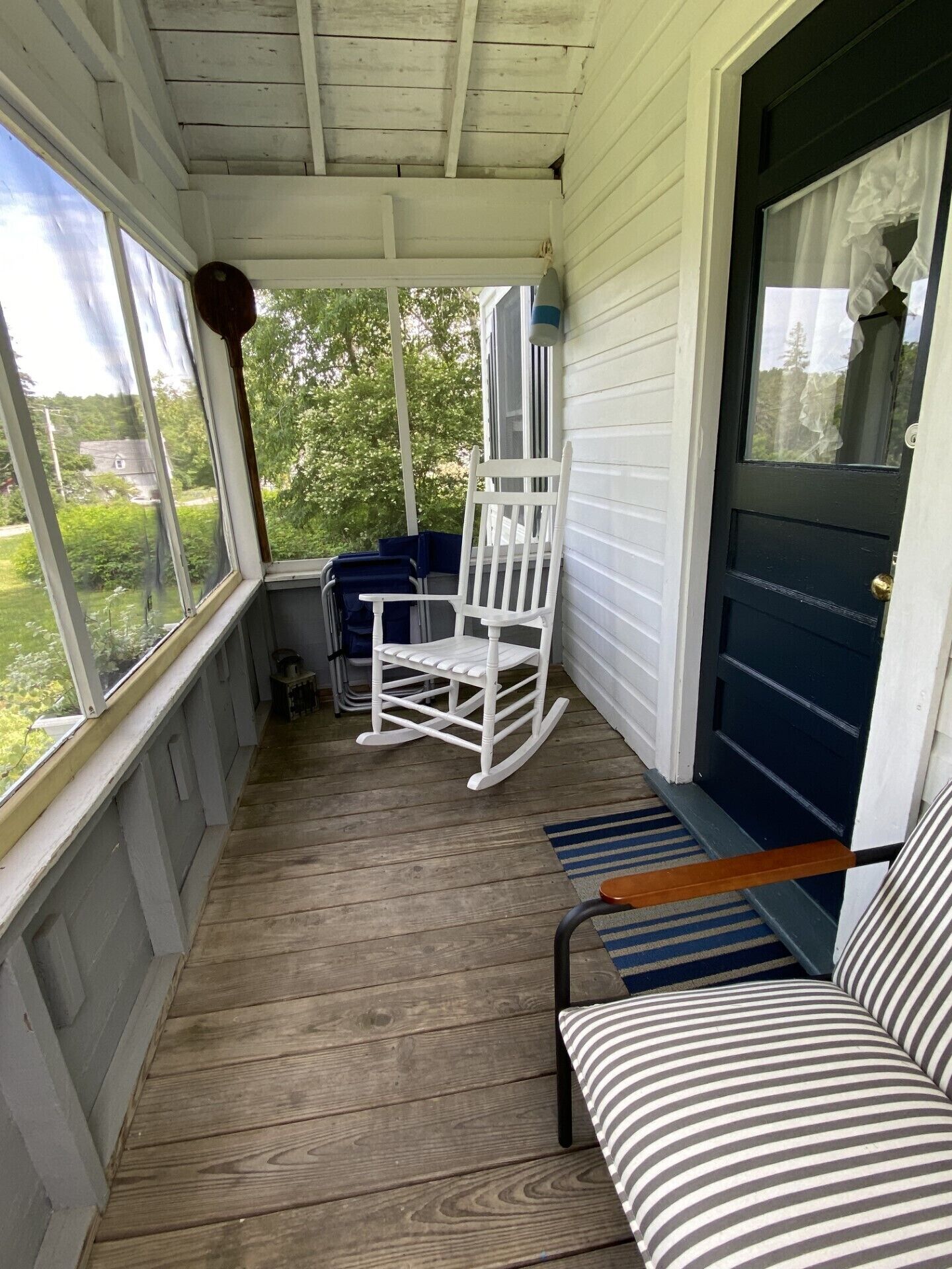 A porch with a rocking chair, a blue bench, and a striped cushion.