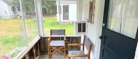 A covered porch with wooden flooring, two folding chairs, a small table, and a black door.