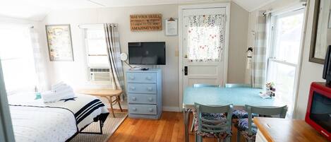 A compact room with a bed, a desk, a chair, a dresser, and a television.