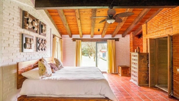 A bedroom with a wooden bed, brick walls, and a large window. - Villa Tinto : Private villa with pool and garden for relaxation and conviviality. (Cuernavaca)