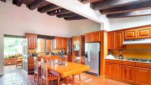 A kitchen with wooden cabinets, a stainless steel refrigerator, and a dining table with chairs. - Villa Tinto : Private villa with pool and garden for relaxation and conviviality. (Cuernavaca)