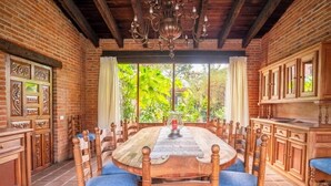 A dining area with a wooden table and chairs, brick walls, and a view of greenery outside. - Villa Tinto : Private villa with pool and garden for relaxation and conviviality. (Cuernavaca)