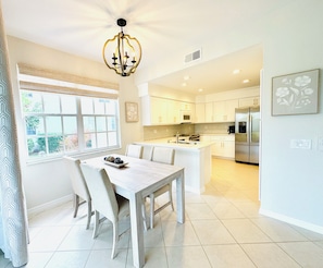 A modern kitchen with white cabinetry, a central island, and a dining area with a table and chairs. - Bonita Bay <Bay Pointe_Unit 103> 2B/2B+Den, 1st Floor, Pond View, 2Car Garage (Bonita Springs)