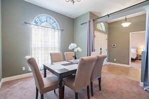 Un coin repas avec une table et des chaises, une fenêtre avec des rideaux et une porte donnant sur une autre pièce.
