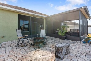 Une terrasse extérieure avec un foyer, deux chaises et une plante en pot.